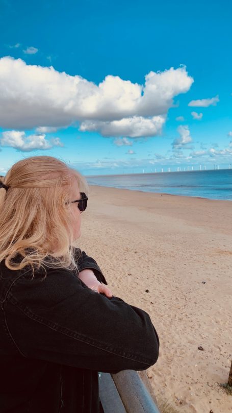Vicki leaning on a railing looking out over a beach at the sea