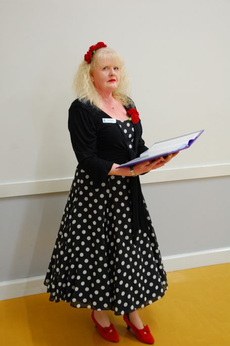 Vicki dressed in a polka dot retro style dress, holding a folder, ready to deliver a ceremony