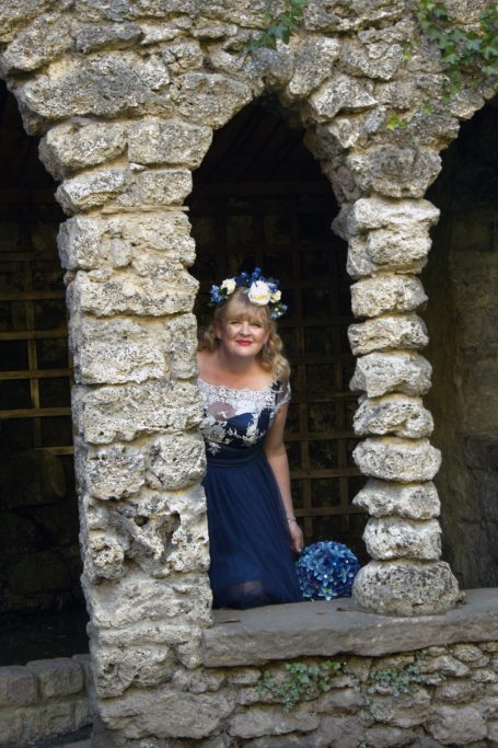 Vicki in a blue wedding dress framed by a stone window at the gardens in Matlock Bath